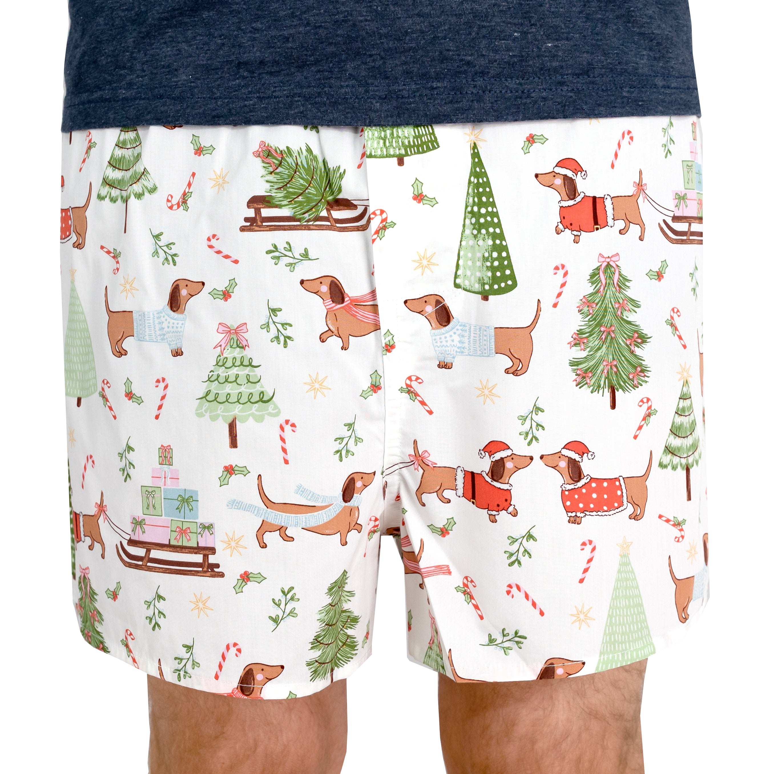 Men's boxer shorts with a white background and a festive Christmas dachshund print, featuring dachshunds in holiday sweaters, Christmas trees, candy canes, and sledding scenes. 