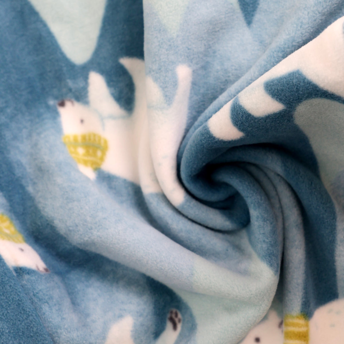 A close-up of a soft fleece blanket with a blue and white polar bear pattern, styled in a spiral fold to show its texture.